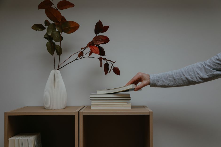 A close-up of a person's hand carefully placing a small decorative vase on a minimalist wooden shelf, representing the final touches of furnishing a home.