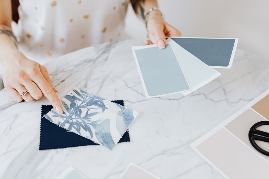 An overhead view of a desk where a person is remotely planning home decor, with a laptop showing a mood board, surrounded by fabric swatches and color palettes.